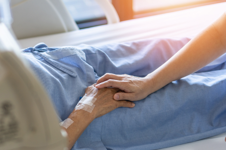 Caregiver is holding the hand of a hospice patient.